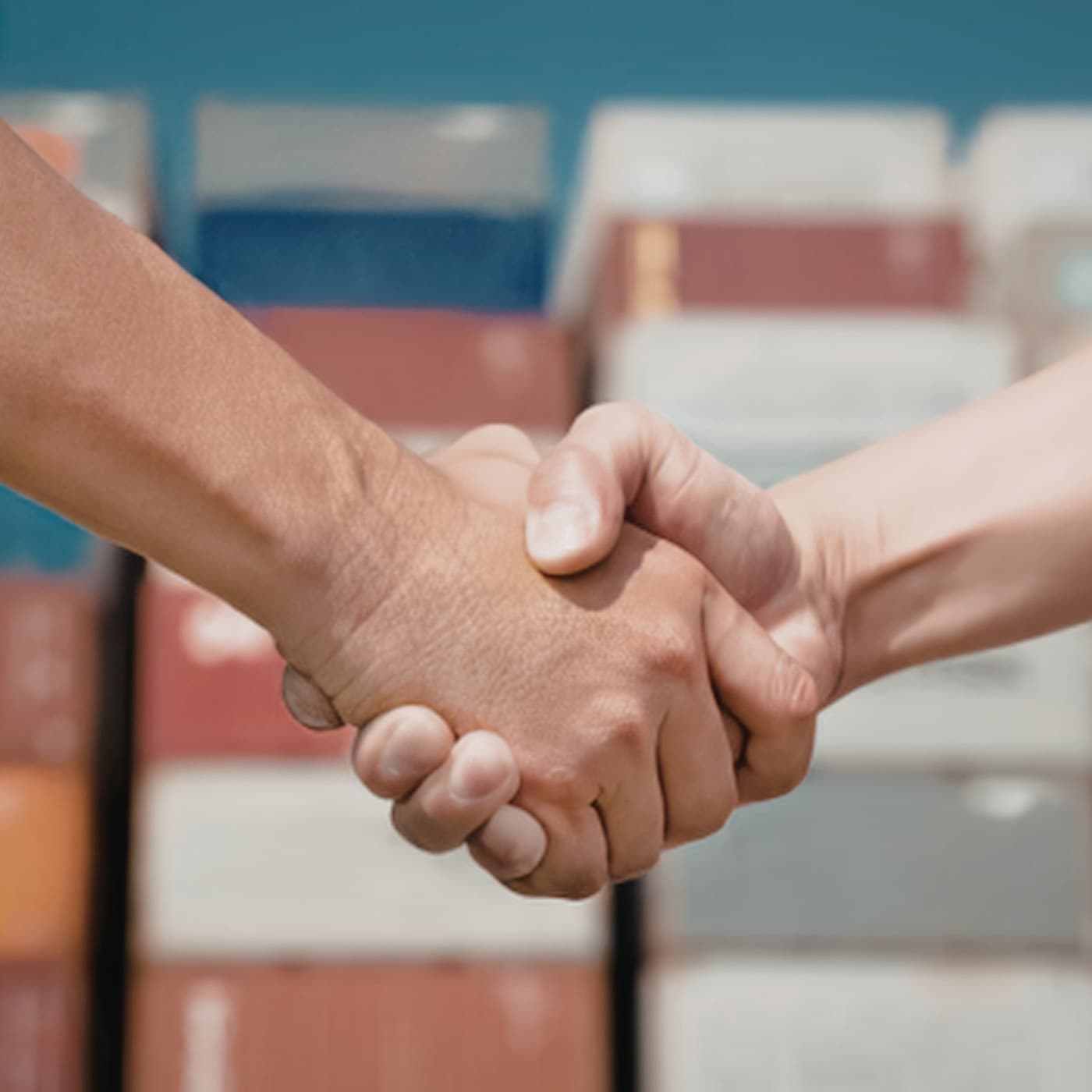 Handschlag zweier Personen vor gestapelten Transportkisten