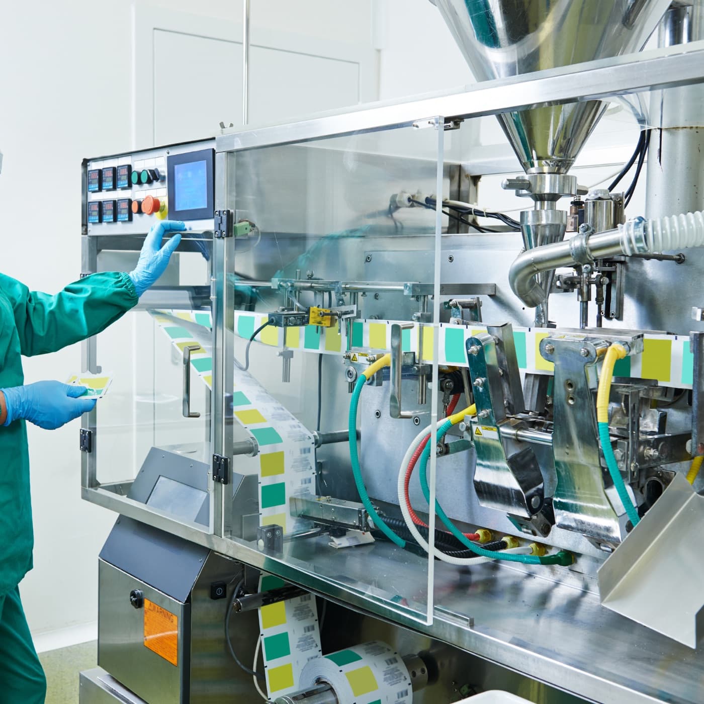 Verpackungsanlage in einem Pharmabetrieb, bedient von einer Mitarbeiterin in Schutzkleidung