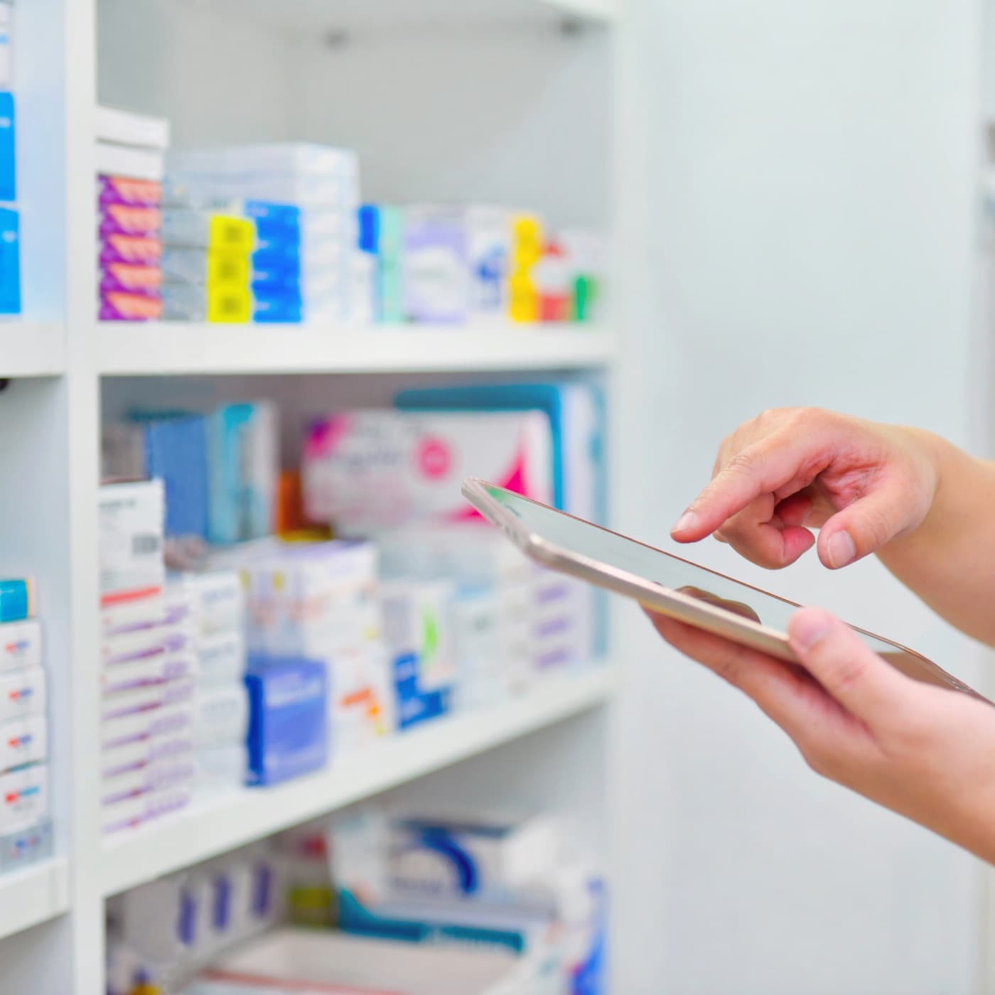 Regal mit Medikamentenpackungen in einer Apotheke, davor eine Hand mit Tablet